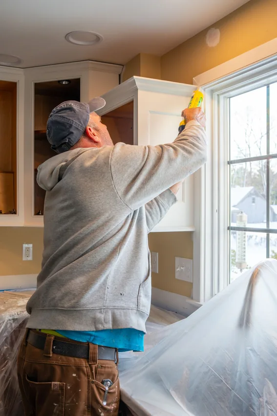 Worker working with caulk at a kitchen cabinet; representative cabinet-repair imagery.