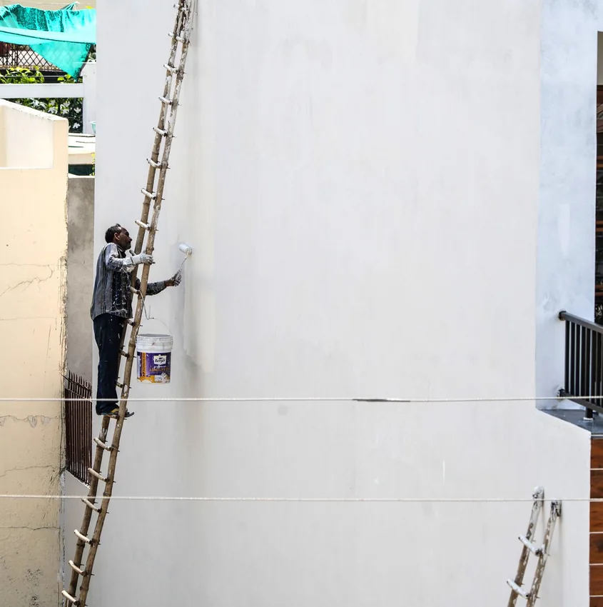 Painter working high on an exterior wall from a ladder.