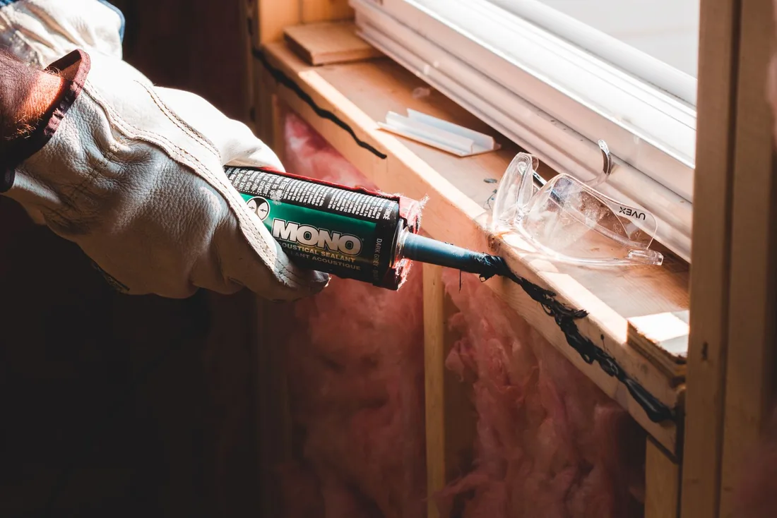 Gloved worker applying sealant along a window seam.