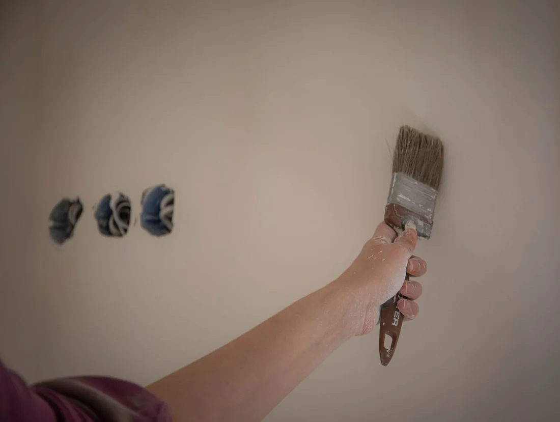 A hand brushing paint onto an interior wall.