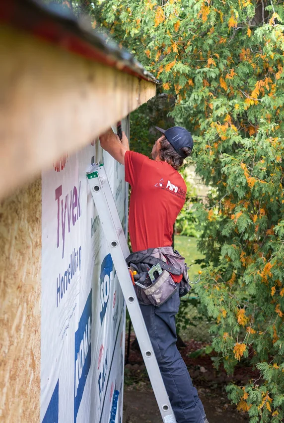Worker on a ladder doing exterior siding and roof repair.