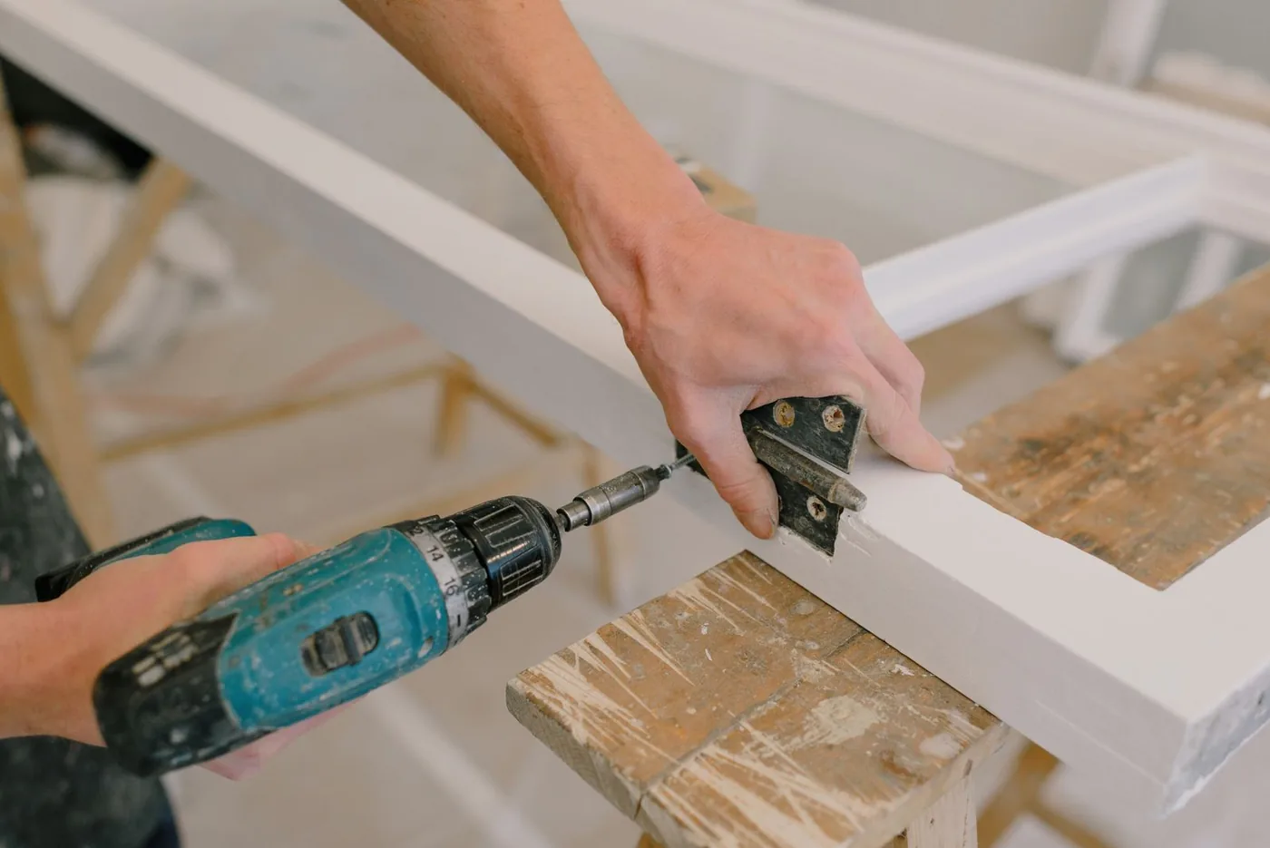 Worker repairing a white wooden window frame with a drill.